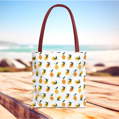Lemon Drop Toss Tote Bag featuring vibrant yellow lemons and green leaves on a white canvas, with long reddish-brown handles, perfect for summer adventures from FireBrook Essentials.