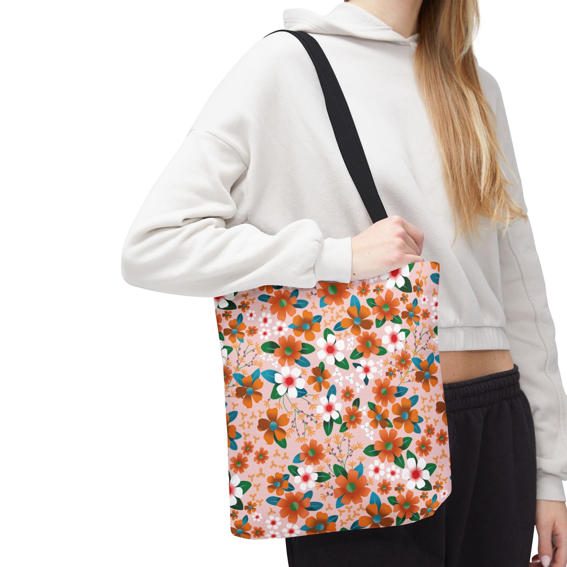 Floral Tote Bag with vibrant orange, white, and teal floral pattern on pale pink, worn by a person with a light-beige cropped hoodie. Ideal for stylish, joyful outings from FireBrook Designs.