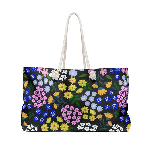 Weekender Bag featuring a black canvas with vibrant floral pattern, thick white rope handles, and a spacious interior, perfect for stylish travel.