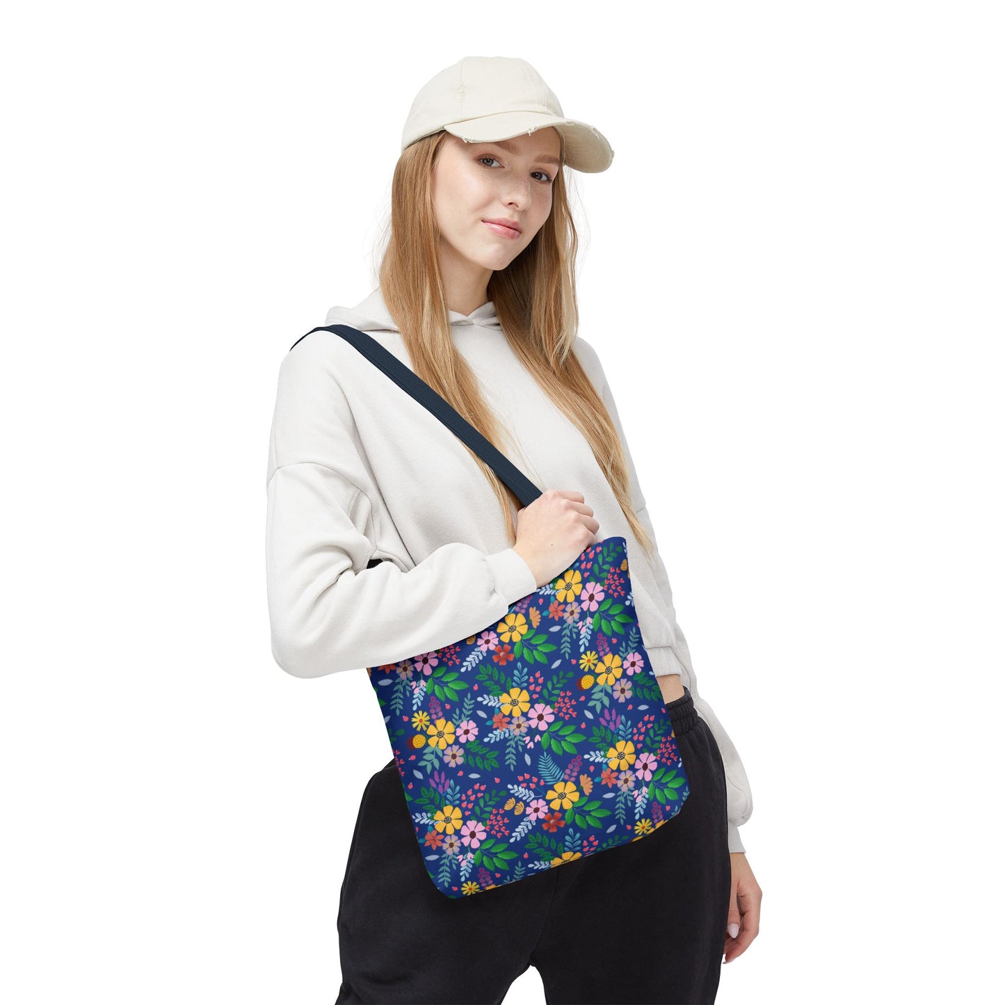 Person with a light-colored cap and hoodie carries the Deep Sea Floral Patch Tote Bag, showcasing its vibrant floral design on a navy-blue background, ideal for joyful, stylish outings.