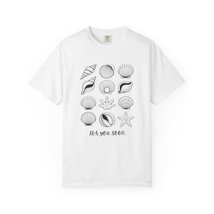 Seashells and Sea You Soon T-Shirt featuring a seashell design and uplifting text, embodies a relaxed beach vibe perfect for ocean lovers, crafted with durable, ethically sourced US cotton for comfort.