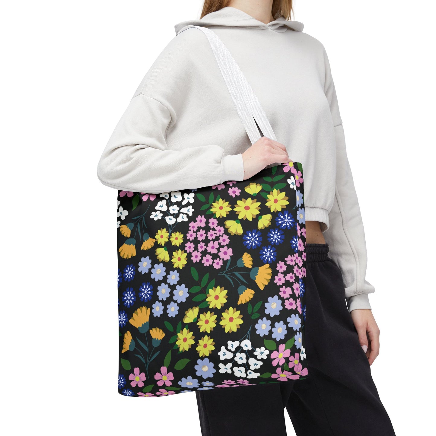 Floral Tote Bag features a vibrant floral pattern against a black background, carried by a person wearing a light hoodie. Ideal for summer activities, it combines durability with cheerful design.