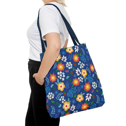 Floral Tote Bag featuring a bright floral pattern on a deep blue background with navy straps, carried over the shoulder of a person in a white T-shirt and black trousers.