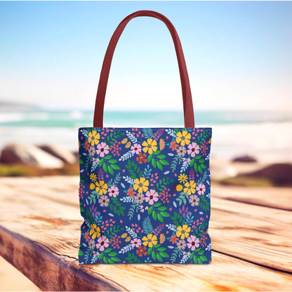 Floral Tote Bag on weathered wood with ocean backdrop, showcasing a vibrant design of stylized flowers and foliage, reddish-brown straps, ideal for joyful summer outings, embodying FireBrook Essentials' uplifting style.