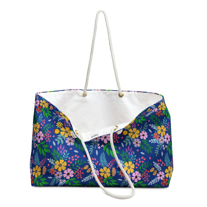 Weekender Bag: A spacious tote featuring a navy-blue floral pattern with vibrant blossoms and green leaves, white rope handles, and a luxurious cream interior, embodying FireBrook Essentials' stylish and joyful design ethos.