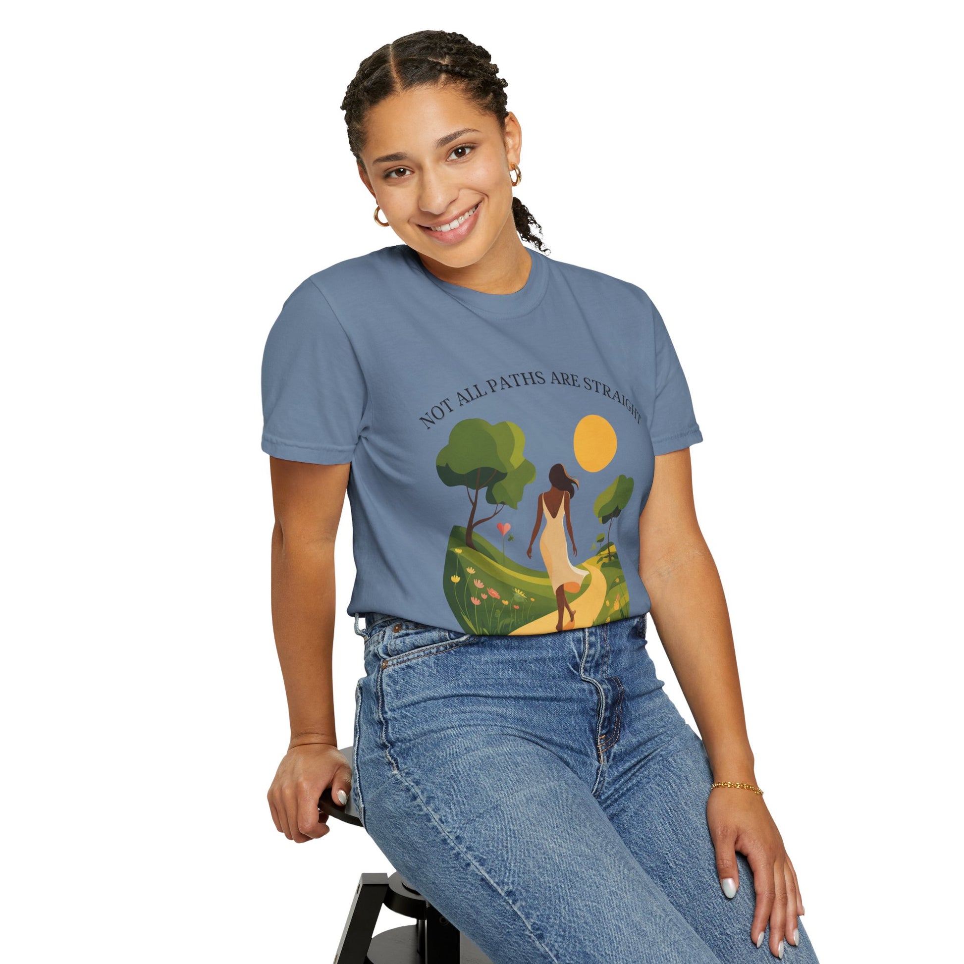Woman wearing the Not All Paths Are Straight Inspirational Message T-Shirt, seated on a stool, smiling, showcasing its relaxed fit and stylish design from FireBrook Essentials.