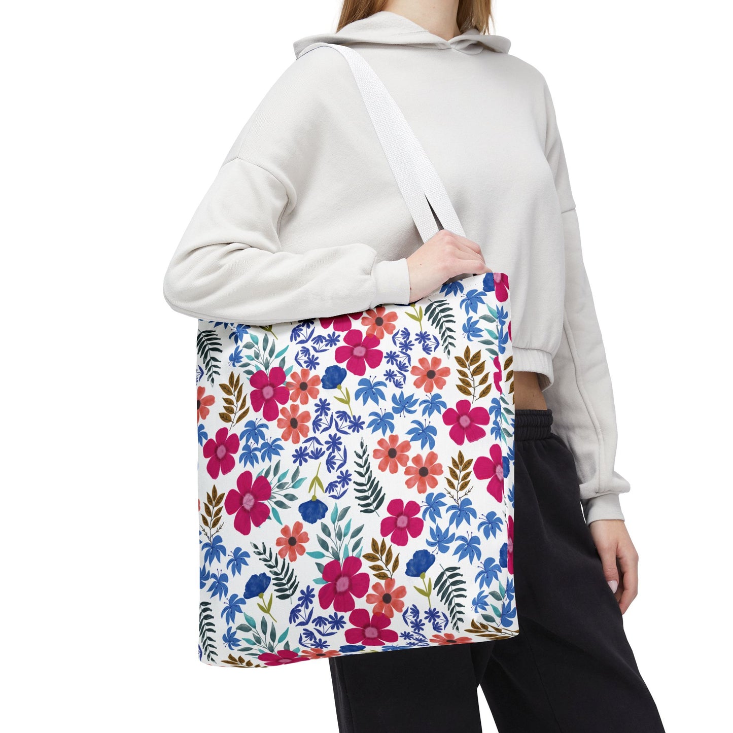 Person wearing a light hoodie and dark pants carries the Confetti Wildflower Tote Bag, featuring a vibrant floral pattern of pink, orange, and blue flowers. Ideal for joyful summer outings.