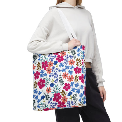 Person wearing a light hoodie and dark pants carries the Confetti Wildflower Tote Bag, featuring a vibrant floral pattern of pink, orange, and blue flowers. Ideal for joyful summer outings.