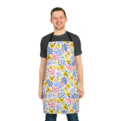 Apron Floral Design features a smiling man wearing a knee-length apron adorned with a vibrant floral print over a dark T-shirt and jeans, embodying FireBrook Essentials' stylish, joyful approach.