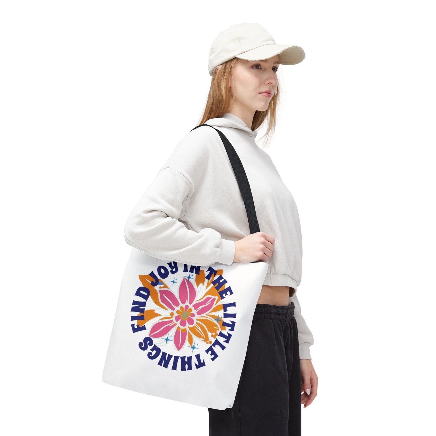Woman in a white hat holding the Find Joy in Little Things tote bag, featuring a flower design.