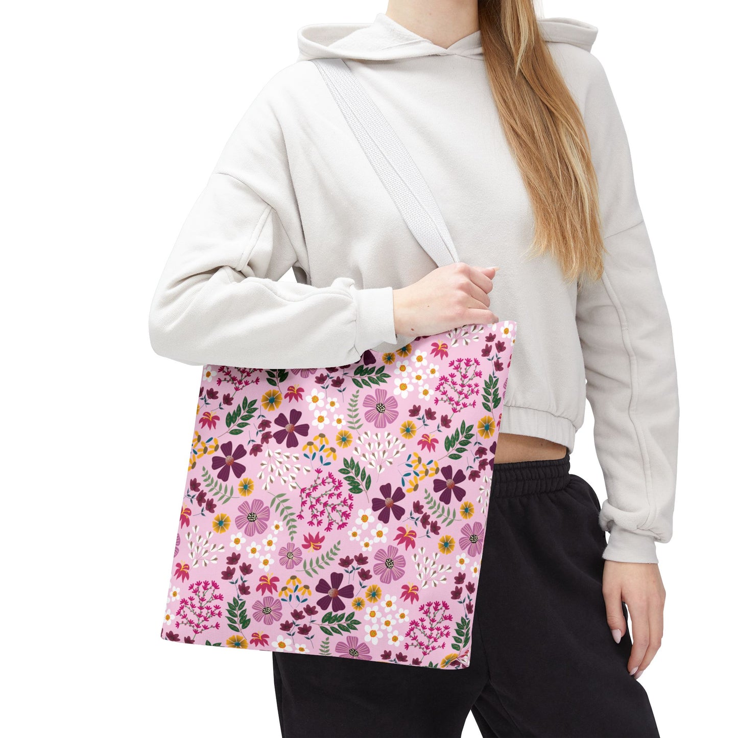 A person wearing a light-beige hooded sweatshirt holds the Rose Garden Blush Tote Bag, featuring a pink floral pattern and light-gray straps, exemplifying FireBrook Designs' stylish and durable accessories.