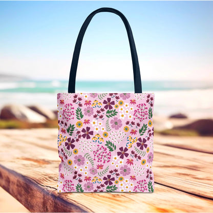 Rose Garden Blush Tote Bag on a wooden surface, featuring a light pink floral pattern with purple and yellow blossoms, complemented by dark navy straps, capturing FireBrook Essentials' stylish and durable design ethos.