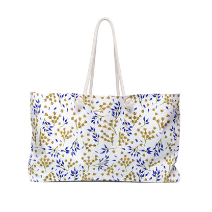 Weekender Bag made from white canvas-like material, featuring knotted rope handles and a botanical pattern of blue and mustard-yellow sprigs, perfectly embodies FireBrook Essentials' stylish, travel-ready design ethos.