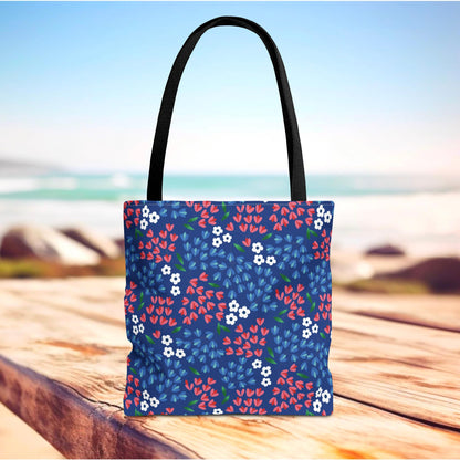 Floral Tote Bag on a wooden surface, featuring a dark blue background with red and white flowers, and black straps. Perfect for summer outings, embodying FireBrook Designs' cheerful and stylish spirit.