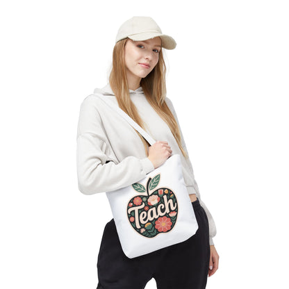Floral Apple Tote Bag features a hand-drawn, pastel-colored apple design with 'TEACH' text, ideal for teachers. Durable 100% polyester with reinforced handles, available in various sizes from FireBrook Essentials.
