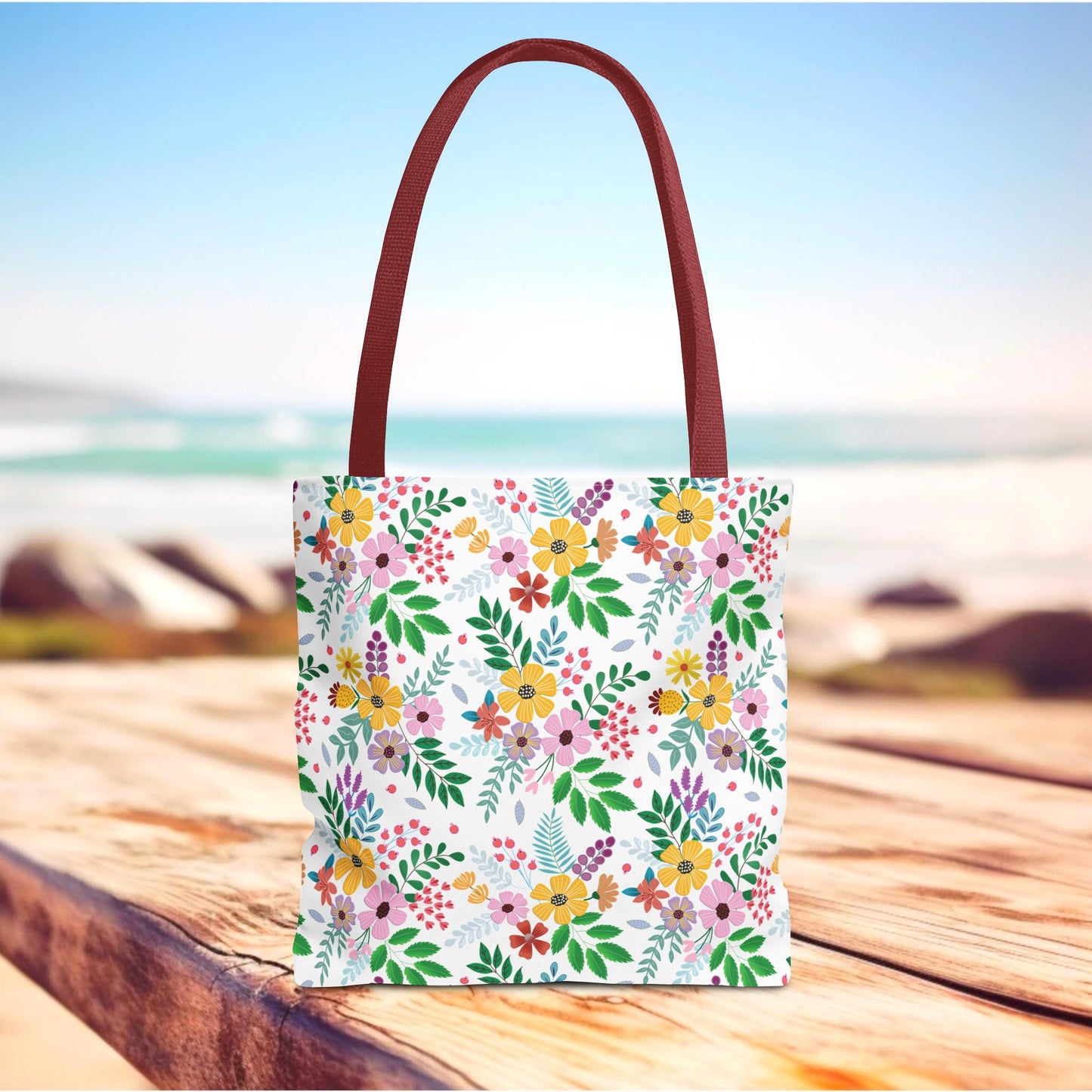 Spring Floral Patch Tote Bag with vibrant floral pattern and reddish-brown handles, standing on a wooden surface, ideal for summer outings or beach trips. Available in multiple sizes, designed for durability and style.