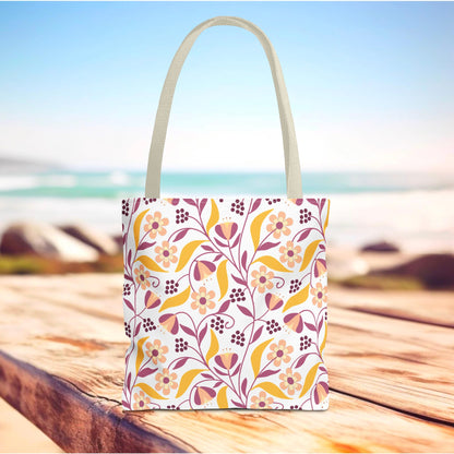 Floral Tote Bag featuring a vibrant floral-and-leaf pattern in pinks, purples, and mustard-yellow, standing on a wooden surface. Ideal for joyful summer outings, with durable polyester and reinforced handles.
