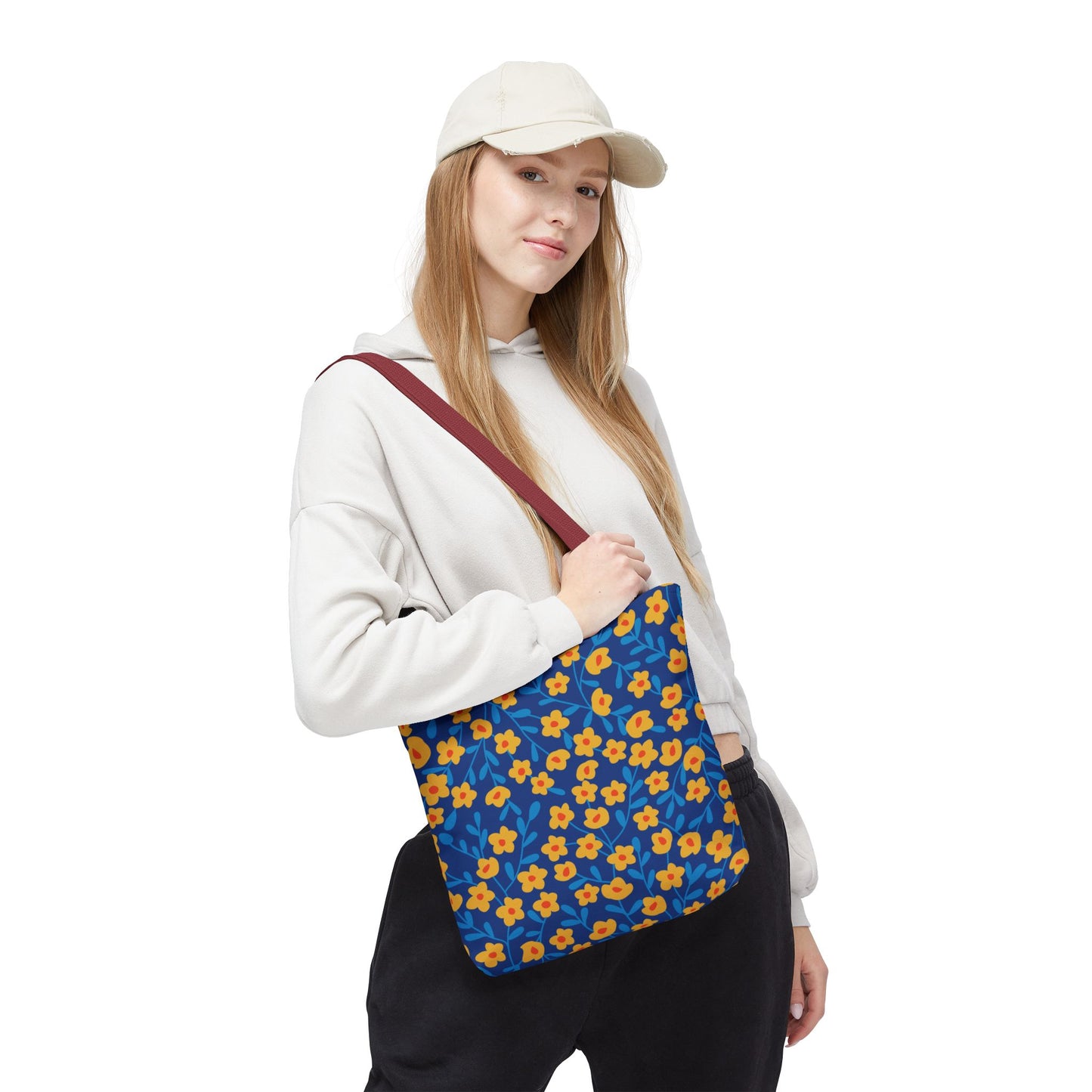 A young woman models the Cobalt Poppy Field Tote Bag, featuring a deep blue base with yellow-orange floral patterns and a burgundy strap, ideal for joyful summer outings.