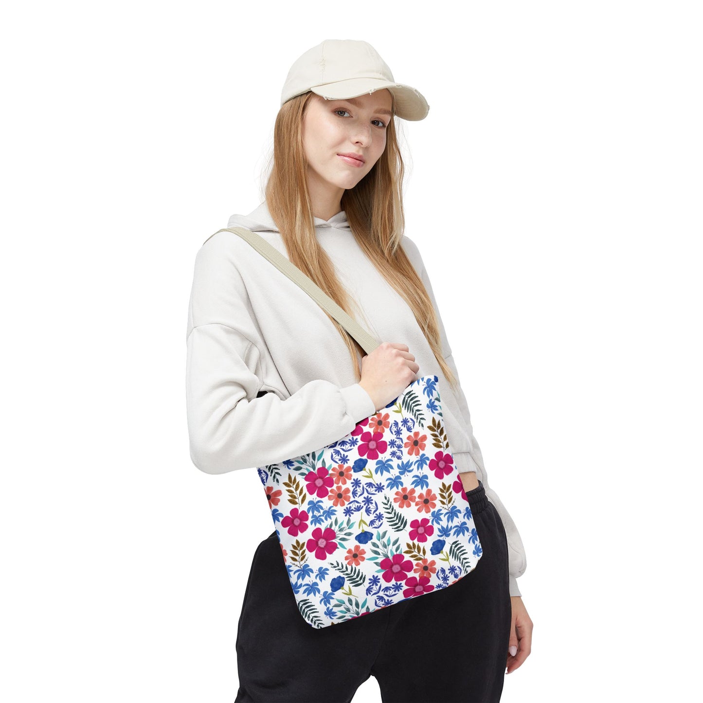 A casually dressed individual holds a Floral Tote Bag, featuring an off-white background with vibrant pink, red, blue, and green floral patterns, embodying FireBrook Designs' cheerful and stylish essence.