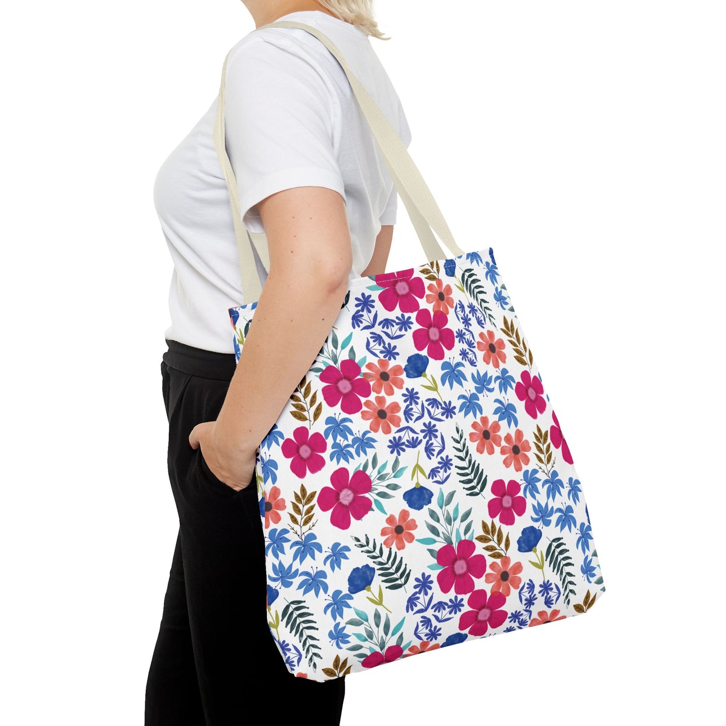 Person holding a Floral Tote Bag with a vibrant hand-painted floral design, featuring pink, coral, and blue flowers. The bag, ideal for joyful summer outings, has a cream-colored strap.