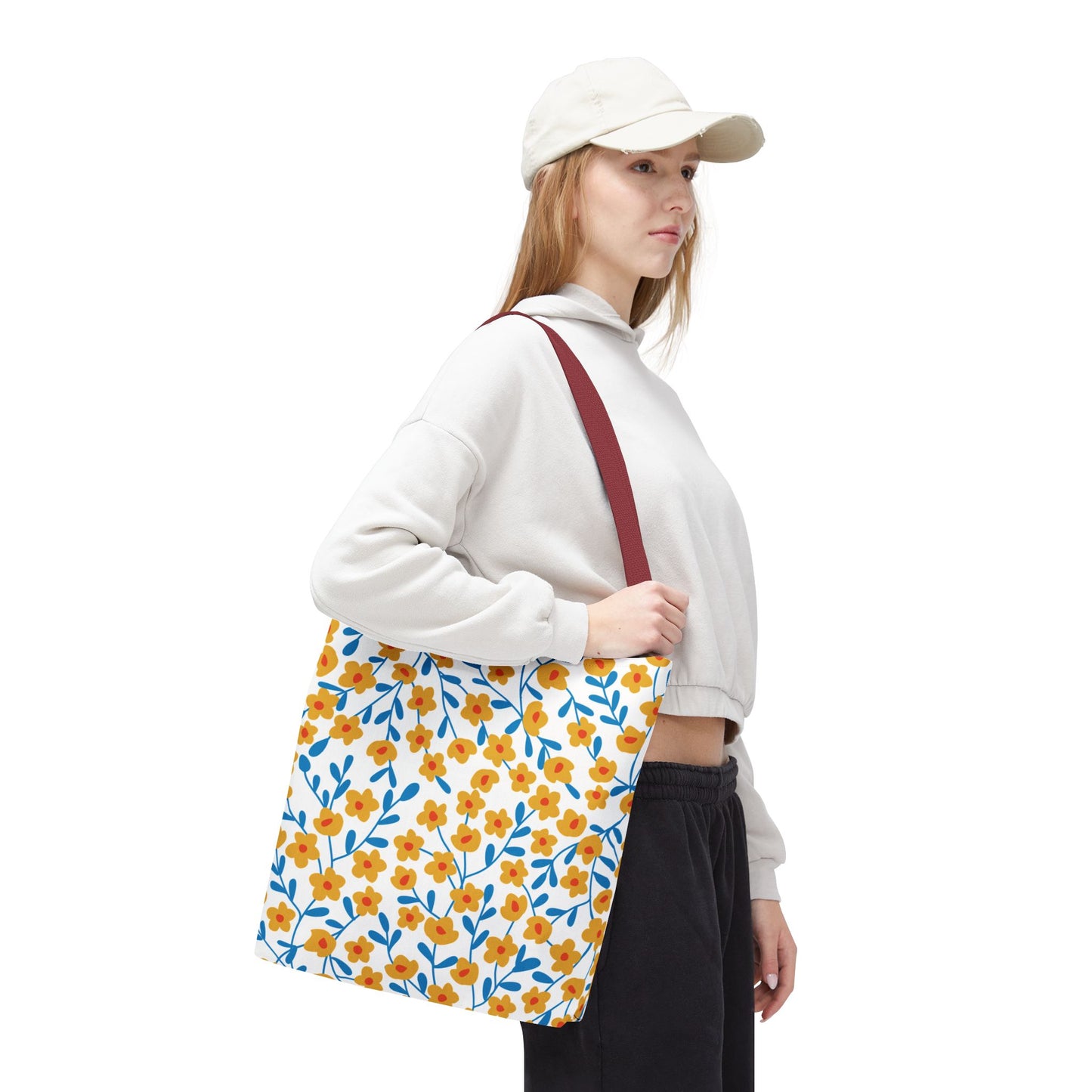 Young woman models the Floral Tote Bag from FireBrook Designs, featuring a cheerful yellow-orange floral pattern with blue accents and a red-wine strap, perfect for joyful summer outings.
