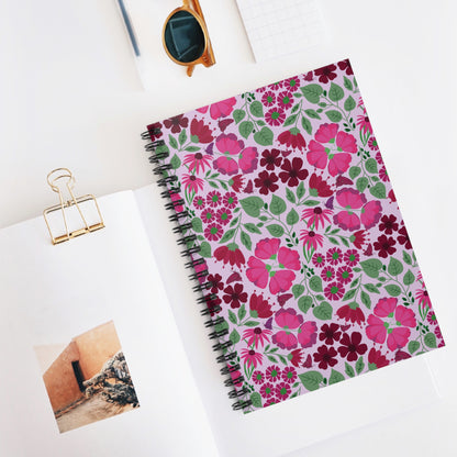 Floral Spiral Notebook with vibrant pink and burgundy flower pattern on a light purple background, surrounded by sunglasses, a small grid notepad, and an open book, reflecting FireBrook Designs' uplifting style.