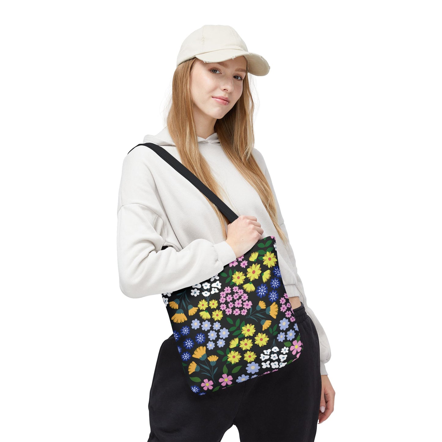 Young woman in light hoodie and cap carries the Starry Night Blooms Tote Bag, featuring a vibrant floral pattern on black. Perfect for joyful summer outings with durable polyester and reinforced handles.