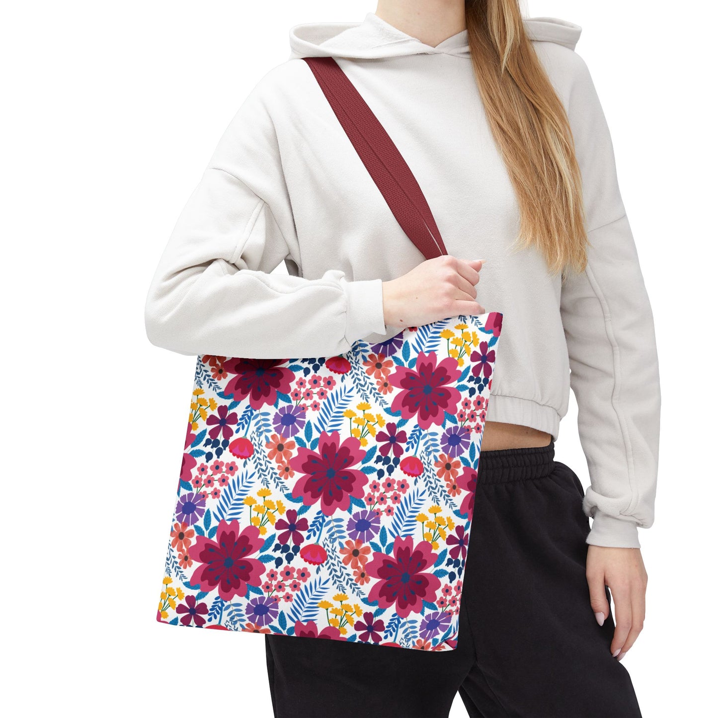 A person wears a light-gray cropped hoodie, holding the Violet Daisy Carnival Tote Bag with burgundy straps, adorned with vibrant floral patterns, embodying FireBrook Designs' joyful, uplifting style for summer outings.