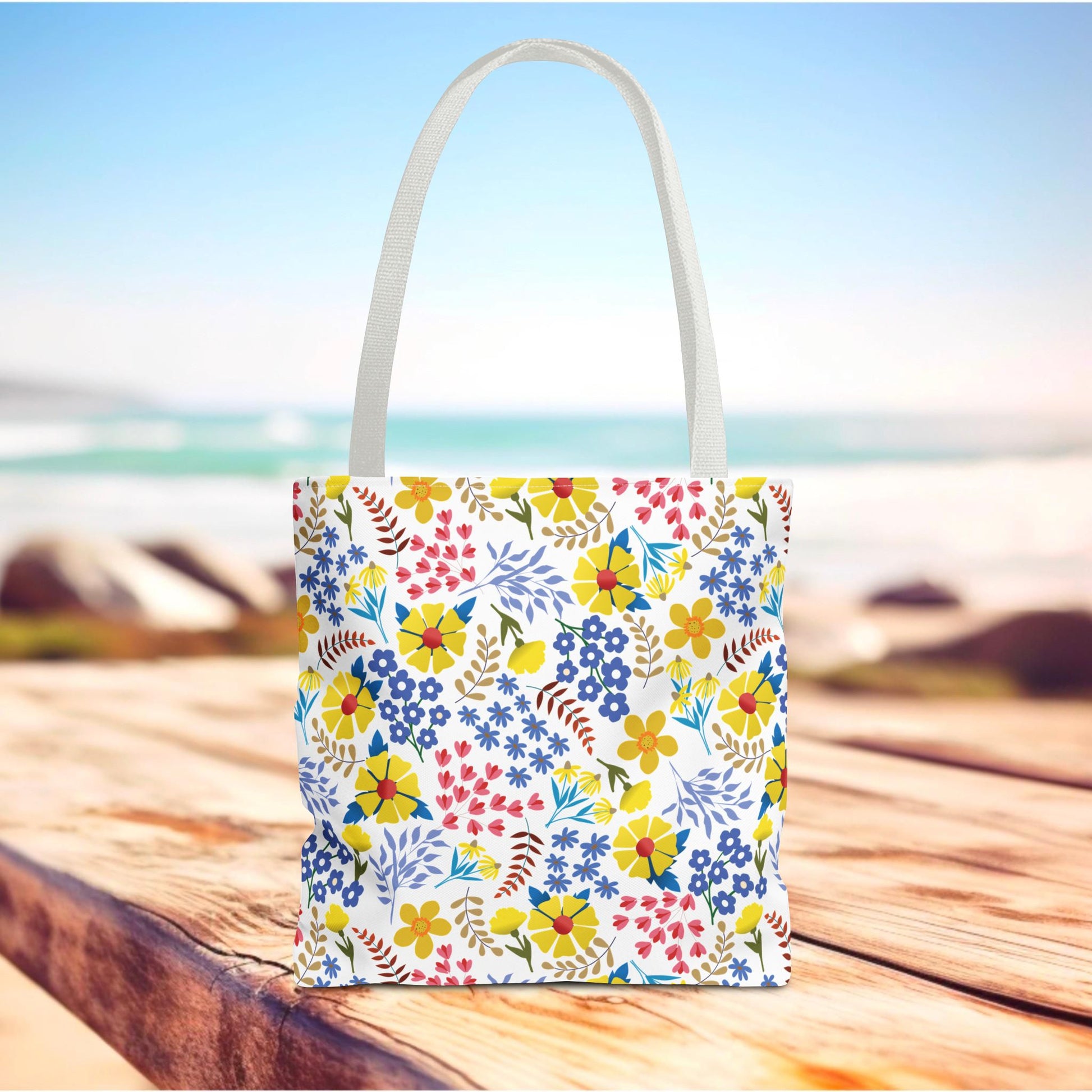 Floral Tote Bag on a wooden surface, featuring a vibrant floral pattern and white handles, perfect for beach or market trips, embodying FireBrook Essentials' joyful and uplifting design ethos.