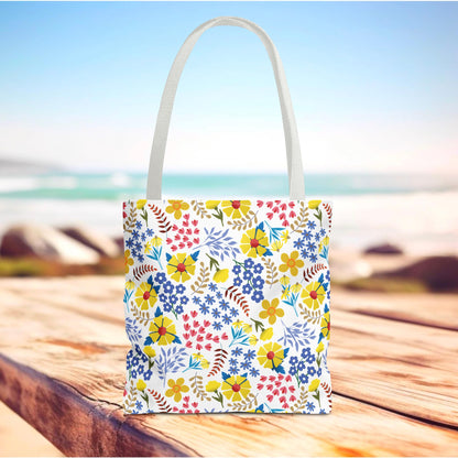 Floral Tote Bag on a wooden surface, featuring a vibrant floral pattern and white handles, perfect for beach or market trips, embodying FireBrook Essentials' joyful and uplifting design ethos.