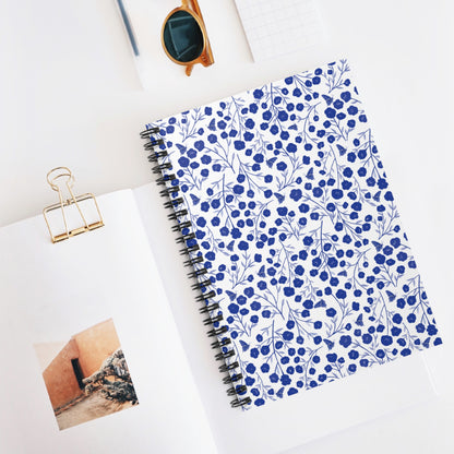 Floral Spiral Notebook with blue flowers and leafy patterns, neatly styled with an open book and sunglasses, epitomizes FireBrook Designs’ blend of style and functionality for creative expression and organization.
