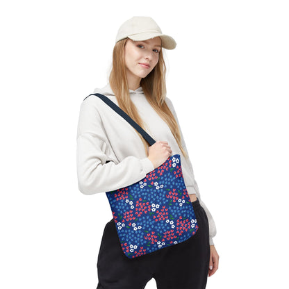 Floral Tote Bag with a navy-blue background, featuring white blossoms, red accents, and blue foliage, carried cross-body by a person in a light hoodie, embodying FireBrook Designs' stylish, uplifting aesthetic.
