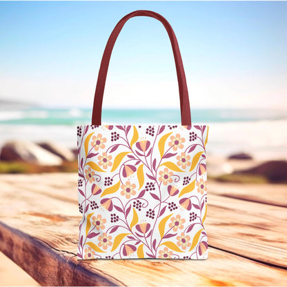 Floral Tote Bag on wooden deck with beach view; features a vibrant pink, mauve, and golden yellow floral pattern, ideal for summer outings. Durable polyester with reinforced handles, designed for style and positivity.
