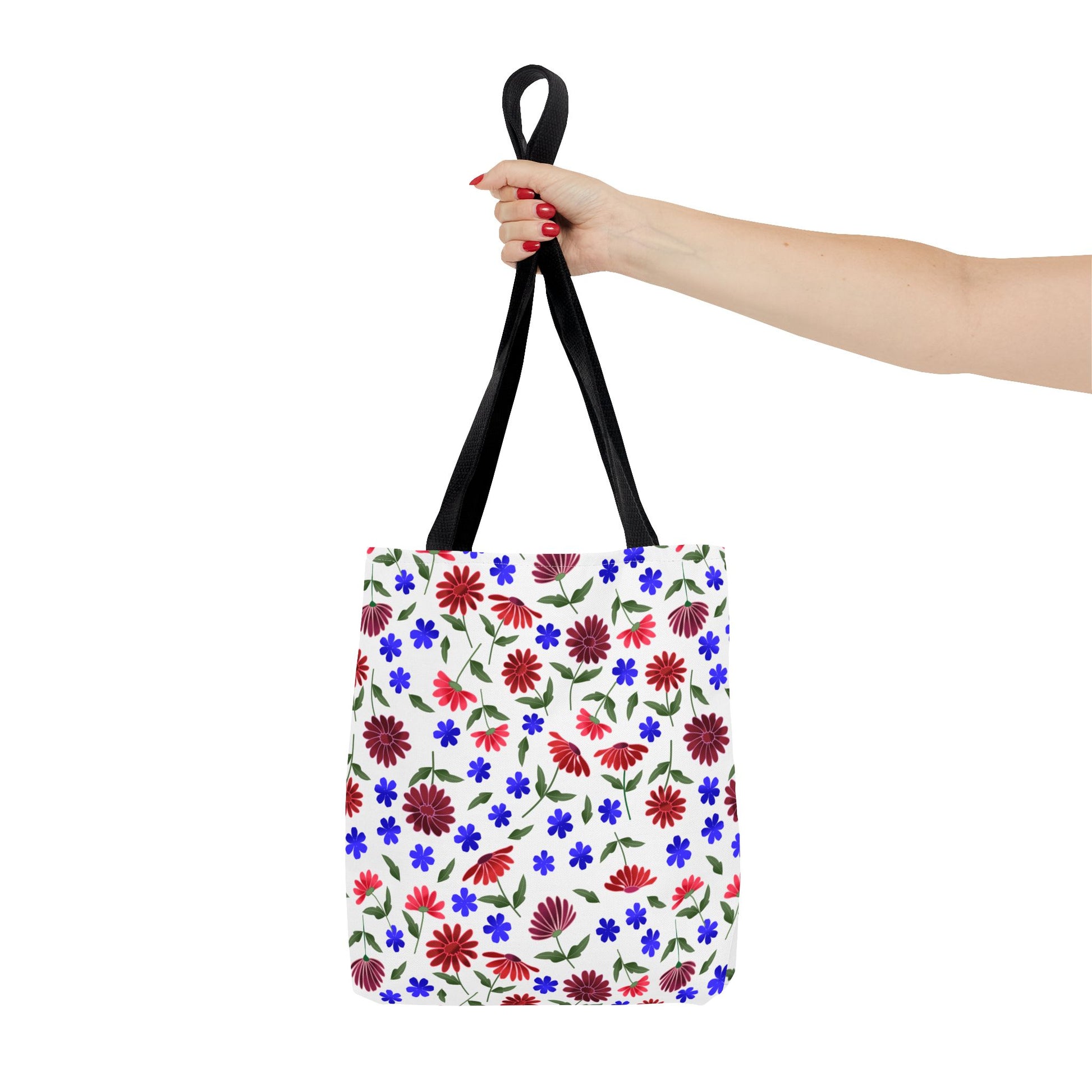 Floral Pattern Tote Bag — Red & Blue Wildflower All-Over Print: Hand holds bag with vibrant red daisies, blue blooms, and green foliage, black straps, embodying FireBrook Essentials' uplifting, practical design.