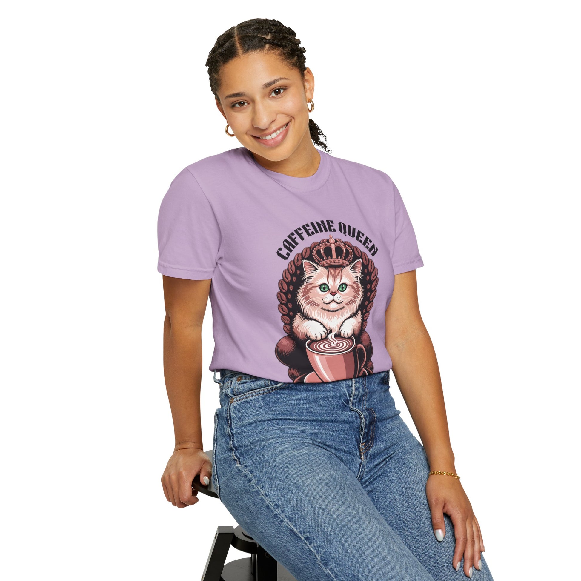 Cat Caffeine Queen T-shirt featuring a cat with a crown and coffee, worn by a smiling woman sitting on a stool, showcasing casual comfort and playful style.