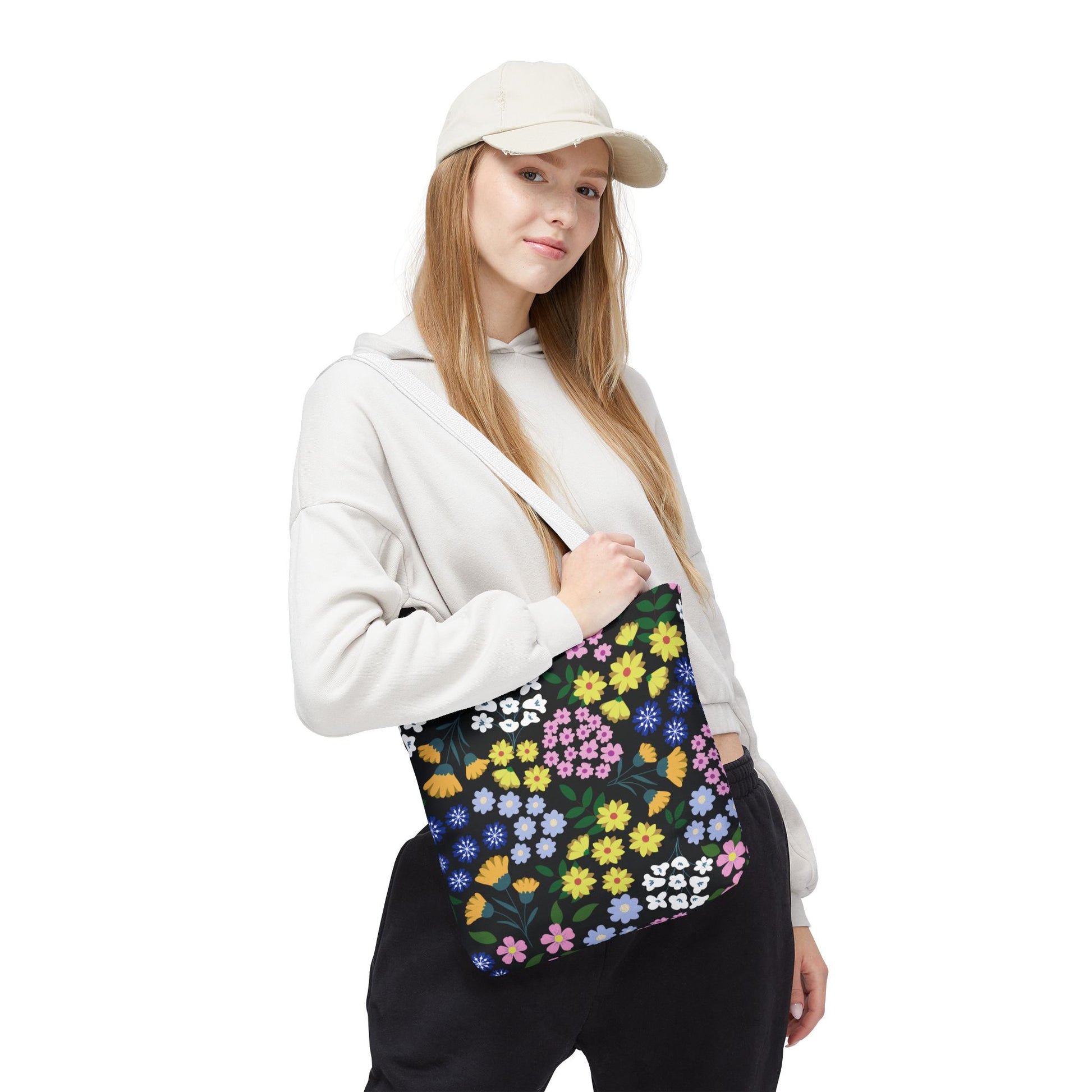 Starry Night Blooms Tote Bag featuring a vibrant, multicolored floral print, held by a young woman in a light hoodie and beige cap. Ideal for joyful, stylish outings, embodying FireBrook Essentials' uplifting designs.