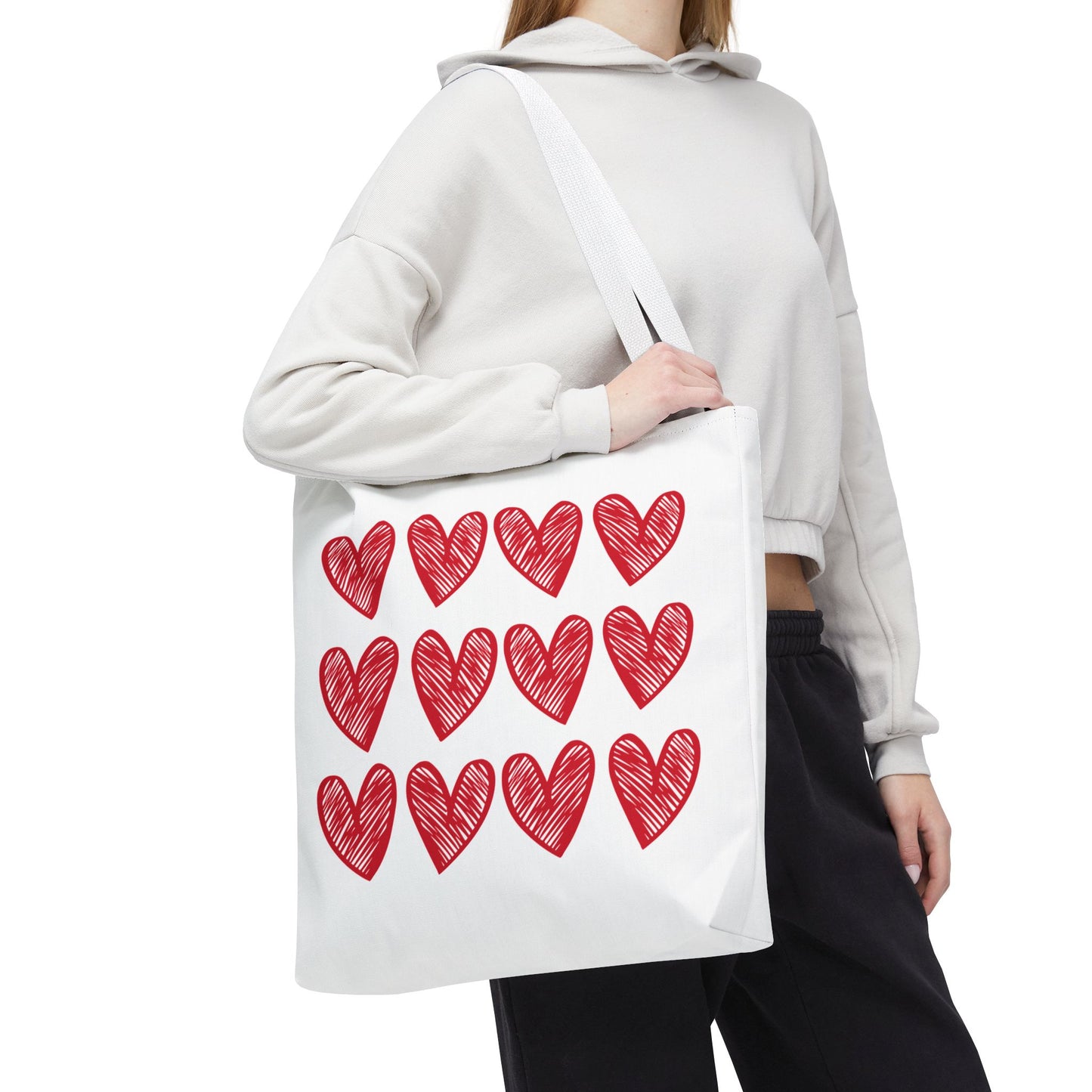 Hearts Tote Bag held by a woman, showcasing its white fabric adorned with red heart patterns. Perfect for adding charm to daily outfits, reflecting FireBrook Essentials' focus on joyful, uplifting designs.
