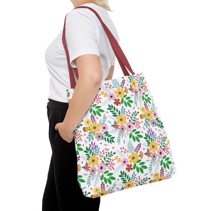 Floral Tote Bag featuring vibrant clusters of yellow, pink, and purple flowers with green leaves on a white background, complemented by deep red straps, perfect for joyful summer outings.