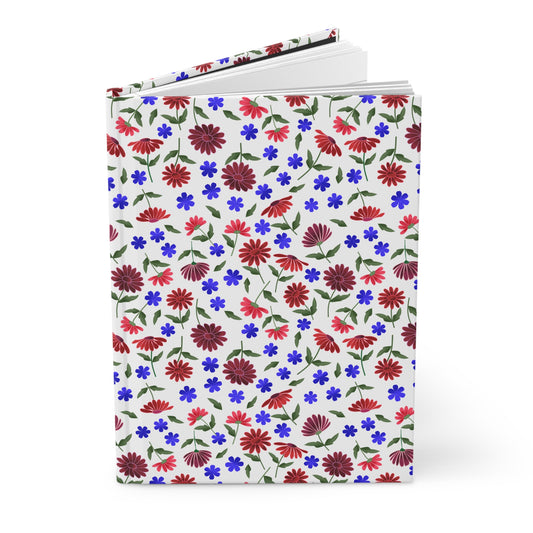 HARDCOVER JOURNAL, MATTE, RULED, 5X7, SEWN BIND, CLEAN-TEAR PAGES – COTTAGE GARDEN, showcasing a vibrant floral cover with daisylike blossoms and blue flowers, standing open slightly to reveal white lined pages.