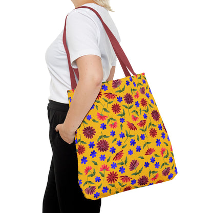 Golden Wildflower Tote Bag with burgundy straps, featuring a vibrant floral pattern on a yellow background, carried by a person in black pants. Perfect for everyday use, combining style and practicality.