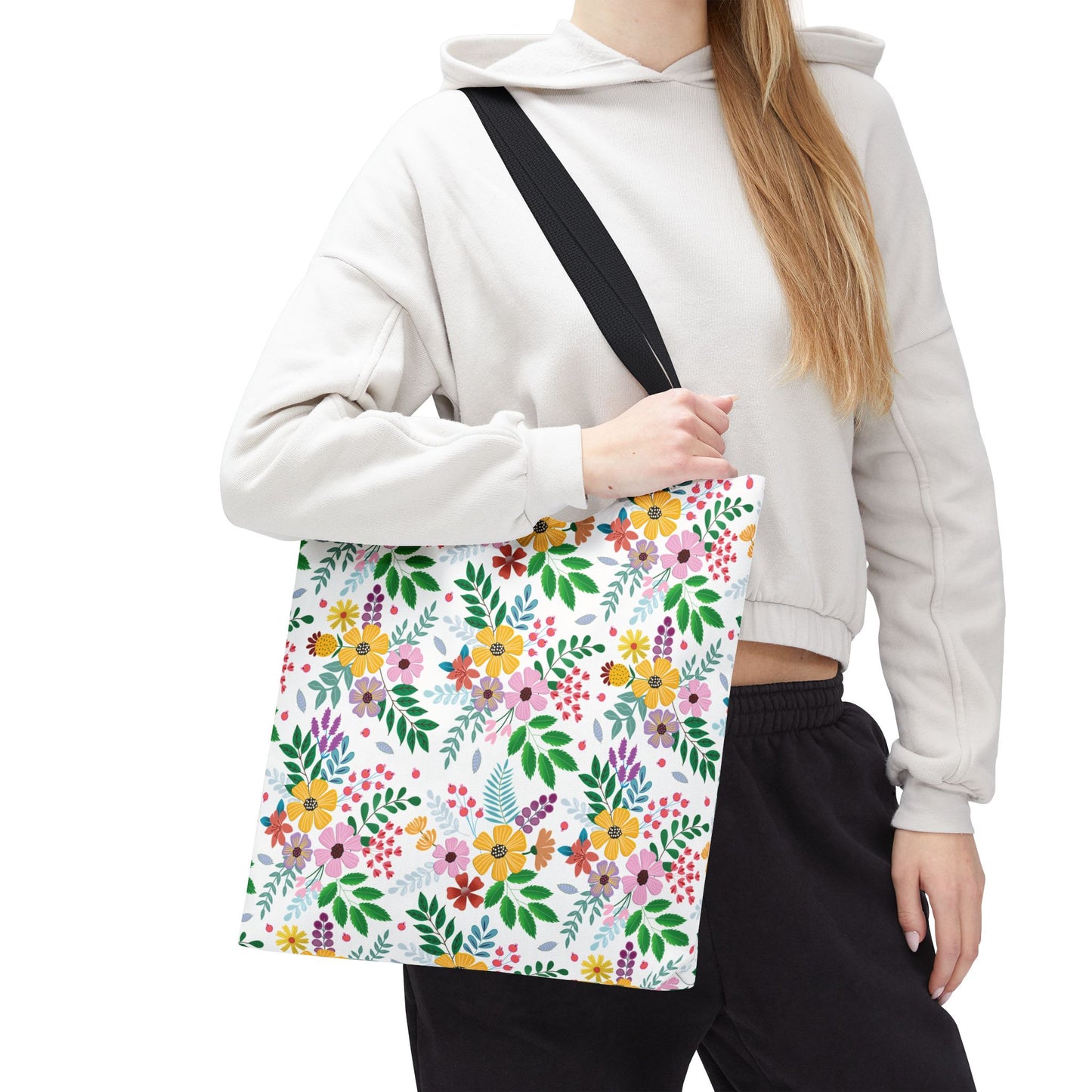 Person wearing a light-gray hoodie and black pants holds the Spring Floral Patch Tote Bag, featuring a vibrant floral pattern and black strap, ideal for joyful summer outings.