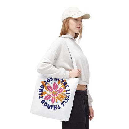 Woman in white hat holds 'Find Joy in Little Things' tote bag featuring a flower design, embodying positivity and versatility for daily use.