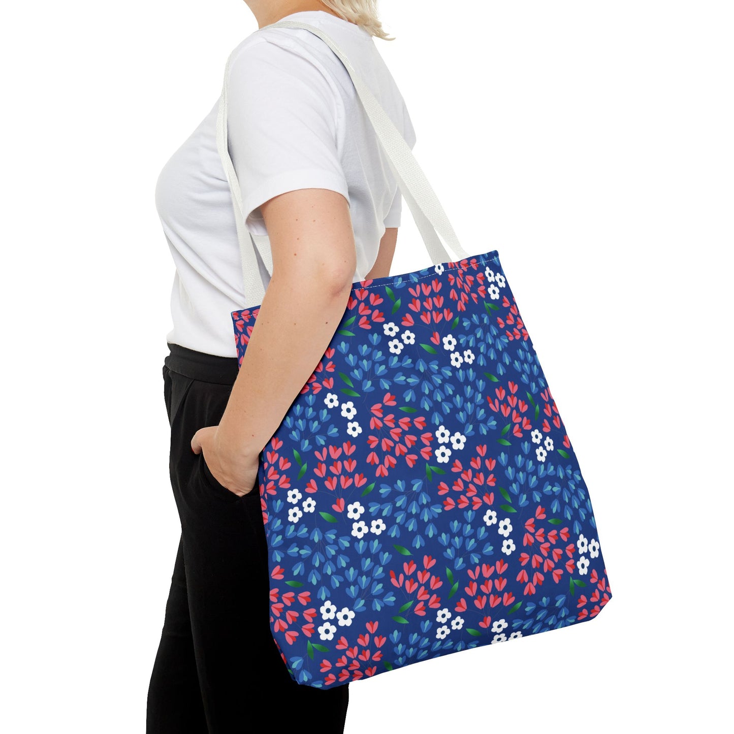 Person wearing a plain white T-shirt and black pants, carrying the Berry Blue Festival Tote Bag with vibrant floral patterns and off-white straps, ideal for summer outings from FireBrook Designs.