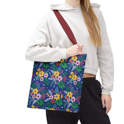 Floral Tote Bag with colorful flower and green leaf pattern, featuring a deep blue background and burgundy-red strap, worn by a casually dressed person. Ideal for bright, cheerful summer outings.