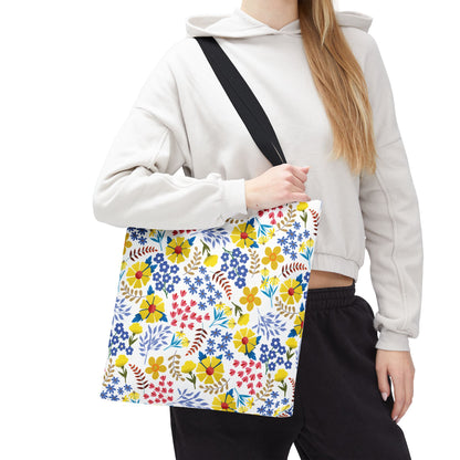 Floral Tote Bag with a vibrant floral pattern in yellow, red, blue, and green, carried by a casually dressed person in a light-beige hooded sweatshirt, highlighting its cheerful, summery design.