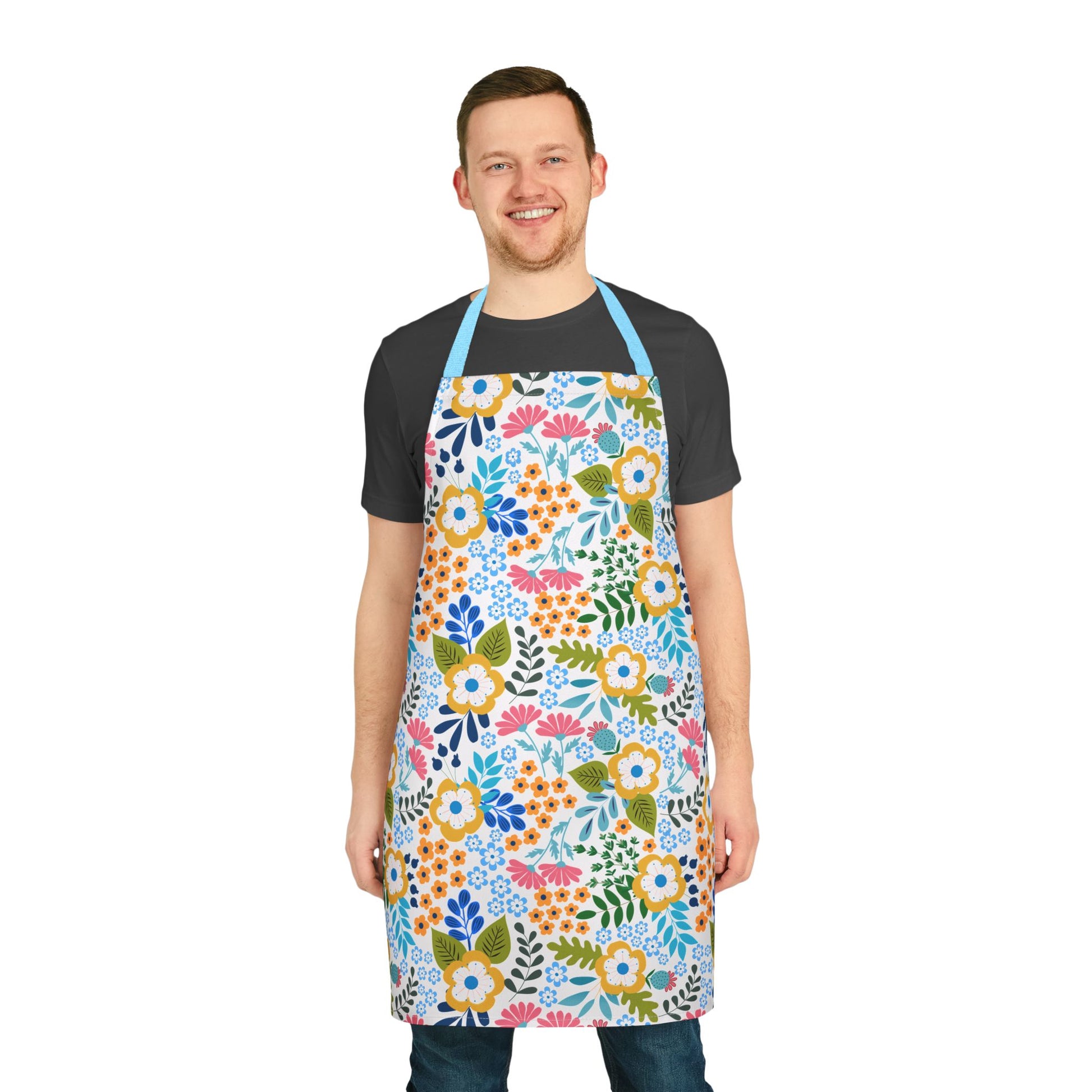 Smiling man models FireBrook Designs' Floral Apron, featuring vibrant flowers and leafy patterns. Crafted from stain-free polyester canvas, it offers a soft, comfortable fit with a light blue neck strap.