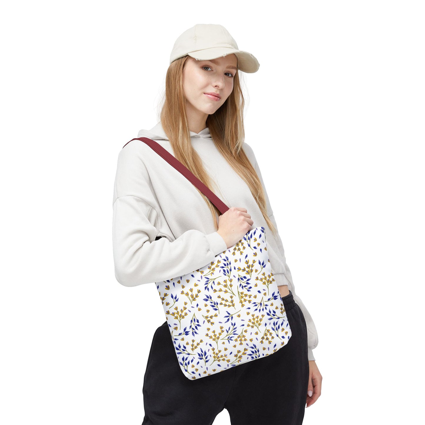 Model with a light cap and hoodie carries a Floral Tote Bag featuring a botanical pattern. The bag has a burgundy strap, ideal for summer outings, aligning with FireBrook Designs' upbeat and practical style.