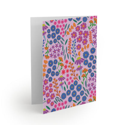 Floral Greeting Cards — Pack of 8/16/24 features a folded card with a whimsical floral pattern on a soft lavender-pink background, perfect for heartfelt messages, accompanied by a matching white envelope.