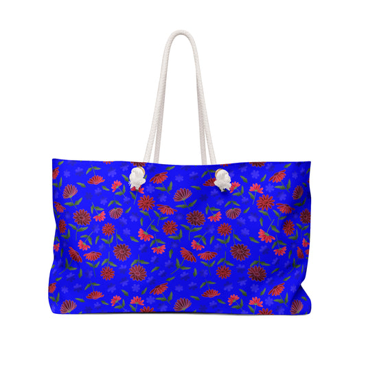 Floral Blue Weekender Bag — Bright Boho Travel Tote features a cobalt-blue canvas with red and pink daisy-like flowers, thick white rope handles, and a spacious design for stylish, joyful travels.