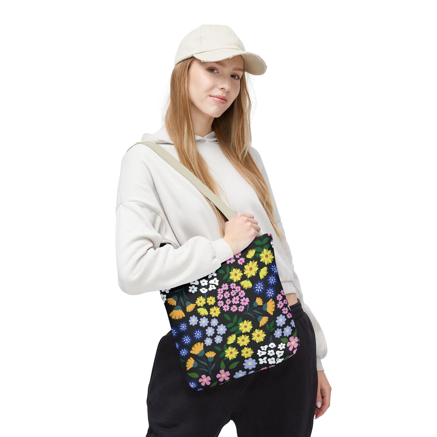 Starry Night Blooms Tote Bag worn by a young woman, features a vibrant floral pattern with yellow, pink, blue, and white flowers on a black background, paired with a casual outfit.